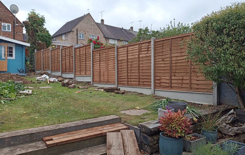 Newly installed wooden fence panels in a garden with potted plants and a blue garden shed