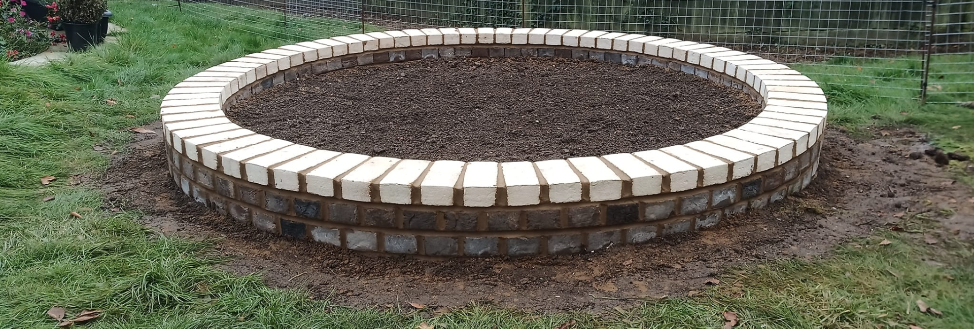 Circular garden bed with brick border on green lawn in enclosed backyard