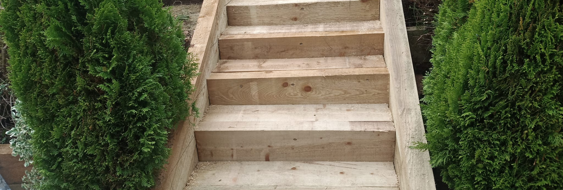Wooden garden stairs with greenery on sides, woodworking tools nearby, outdoor landscaping project in progress