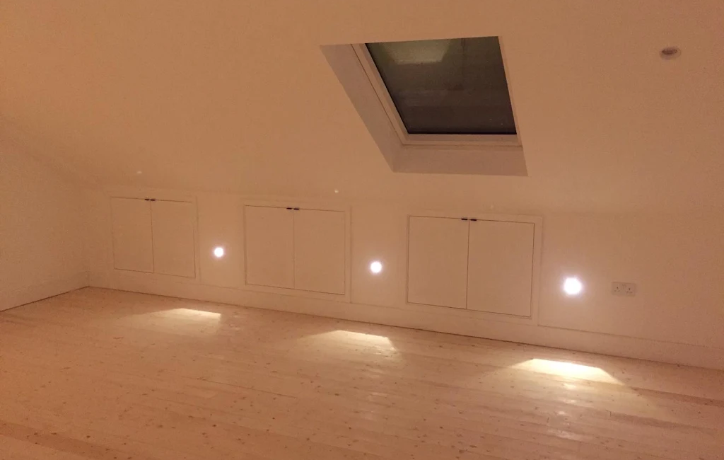 Minimalist attic room with skylight, recessed lighting, and wooden flooring, highlighting simple design and storage spaces