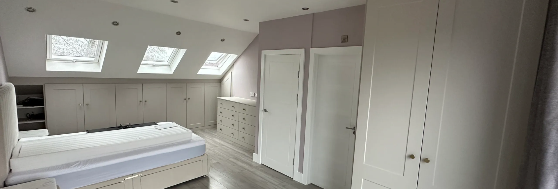 Spacious attic bedroom with skylights, modern cabinetry, and neutral tones, featuring a comfortable double bed