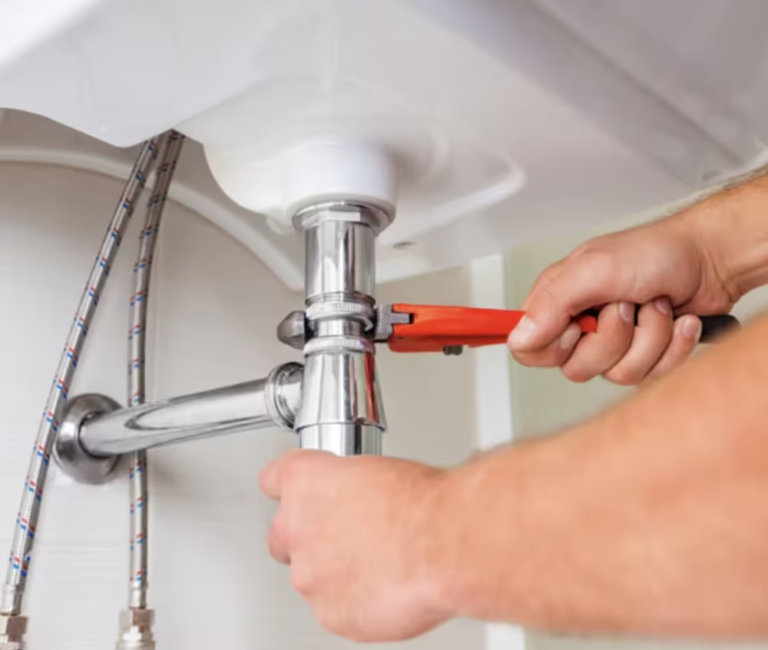 Plumber using a wrench to fix a sink pipe under a bathroom basin, showcasing plumbing repair and maintenance skills