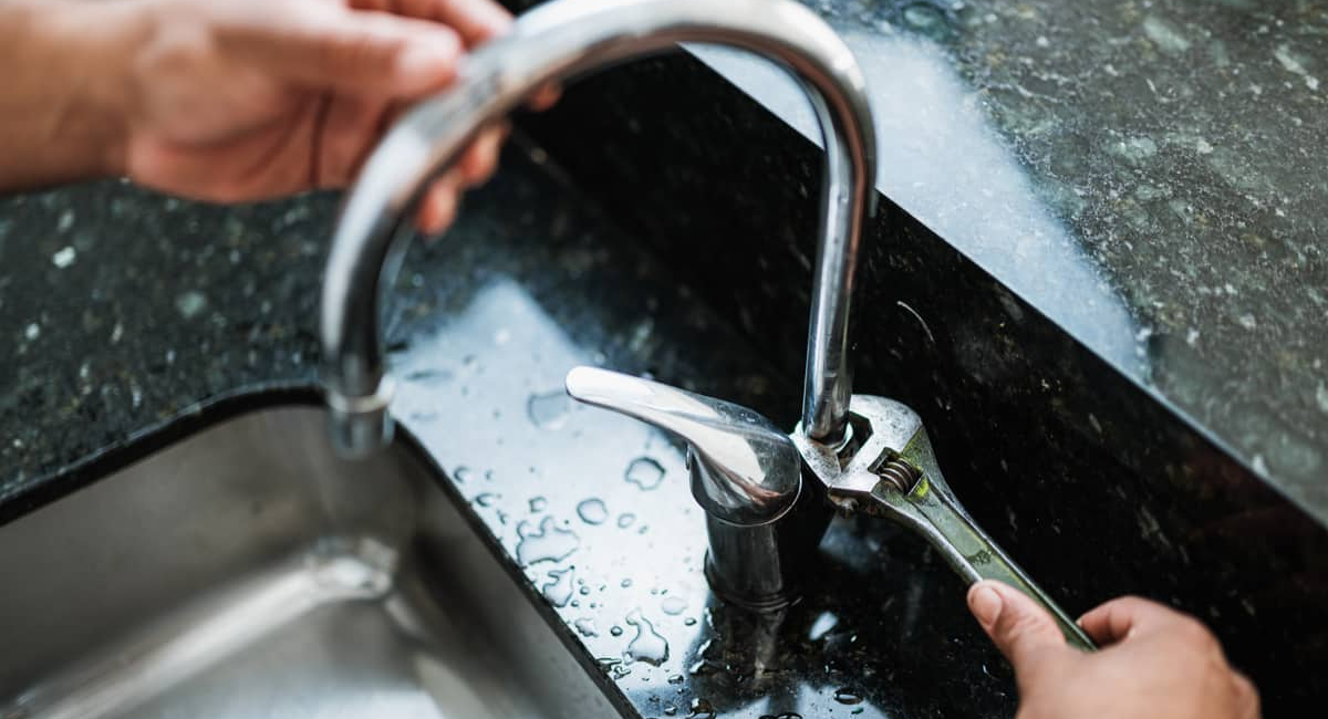 Person using a wrench to repair a leaking kitchen tap on a black countertop