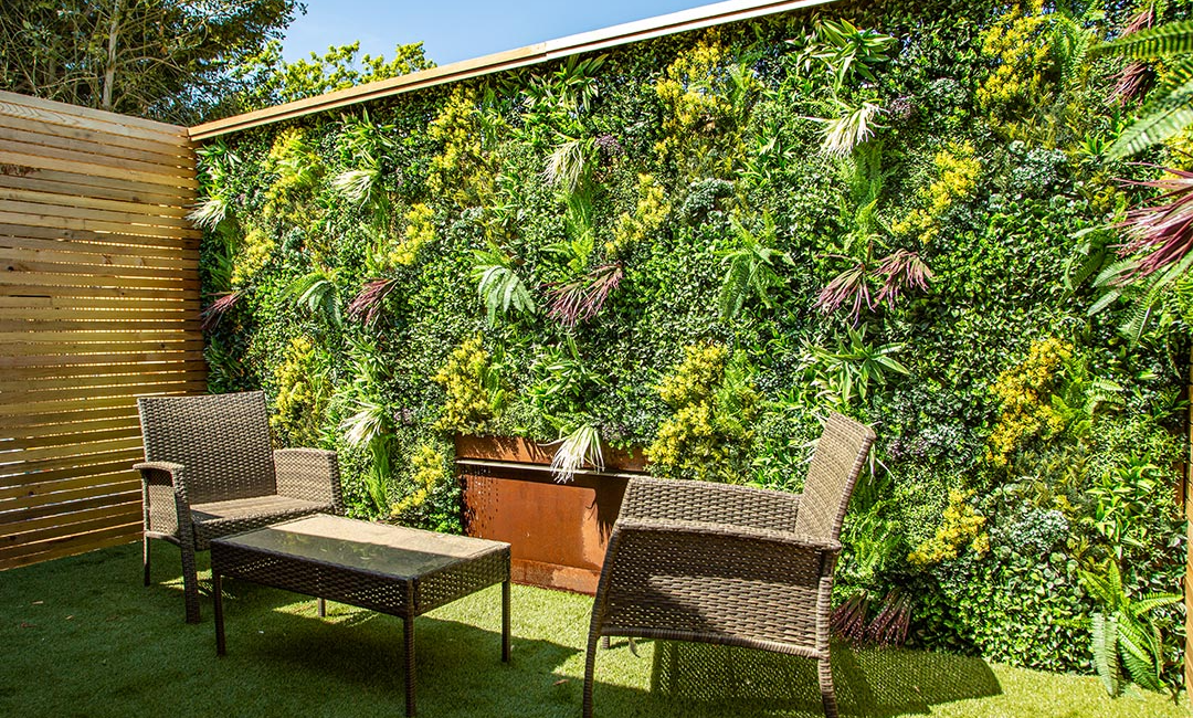 Outdoor seating area with wicker chairs and table against a lush vertical garden wall in a sunny patio setting