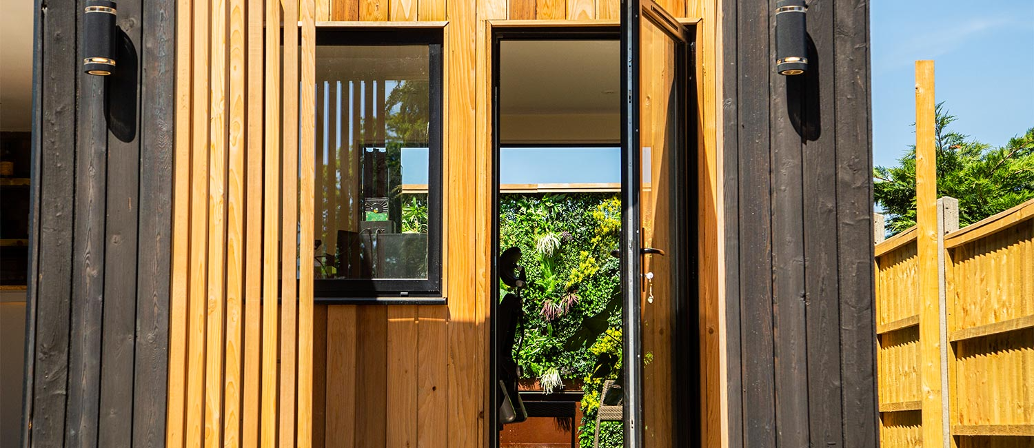 Modern garden room exterior with open door revealing green living wall inside