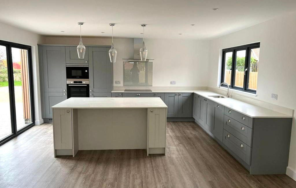 Modern kitchen with grey cabinets, central island, pendant lights, and large windows for natural light