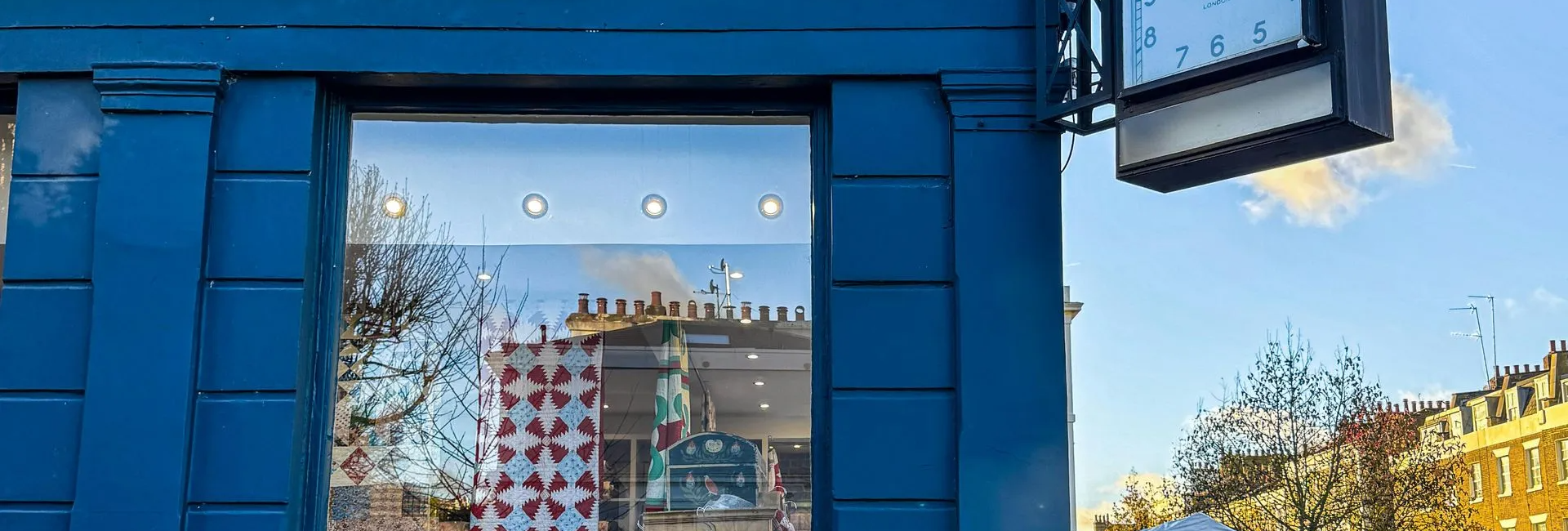 Storefront of Antique Textiles Company with a vintage clock and colourful quilts displayed inside a blue building