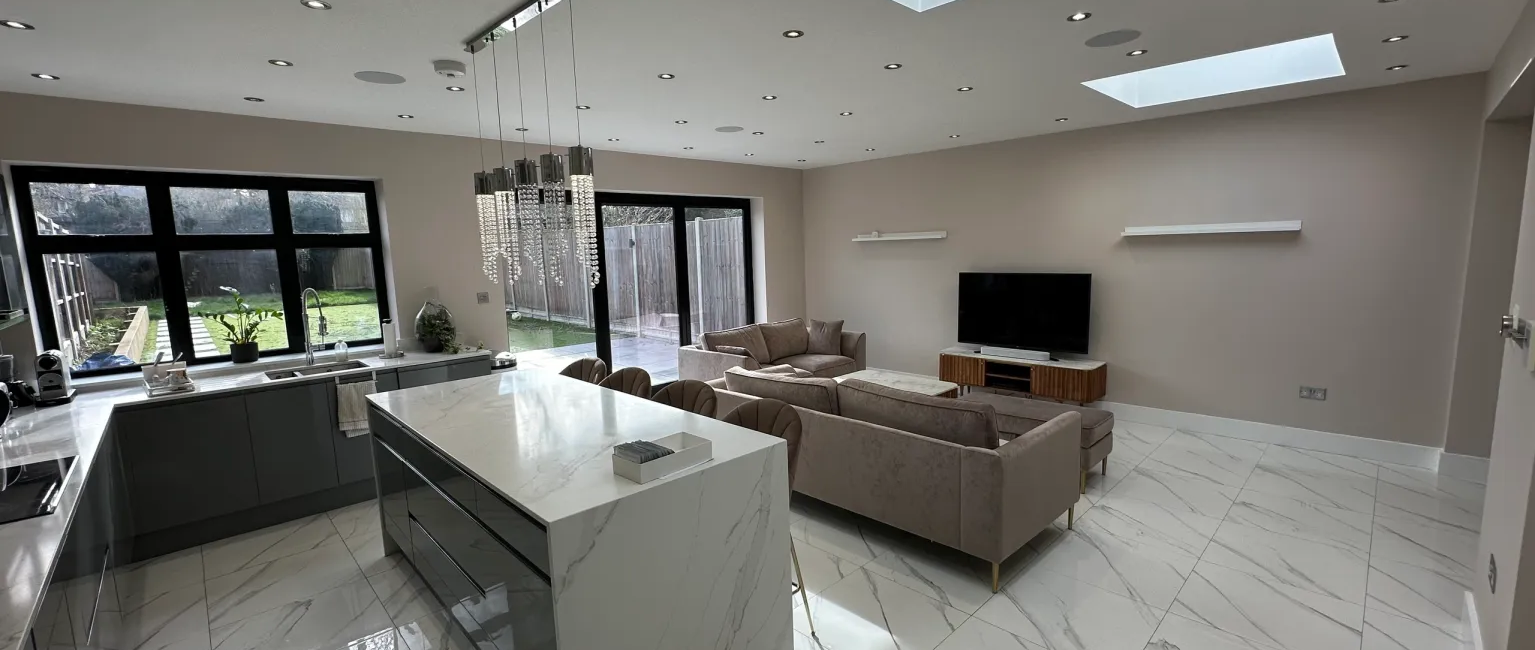 Modern open-plan kitchen and living area with marble flooring, skylights, and large windows overlooking the garden