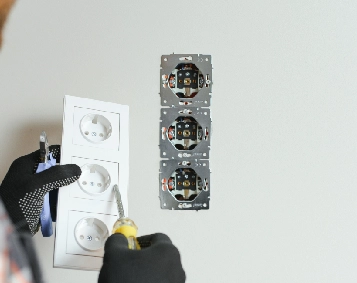 Electrician installing triple power sockets on a wall using tools