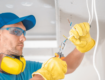 Electrician wearing safety gear installing ceiling wiring in a building site for efficient electrical solutions