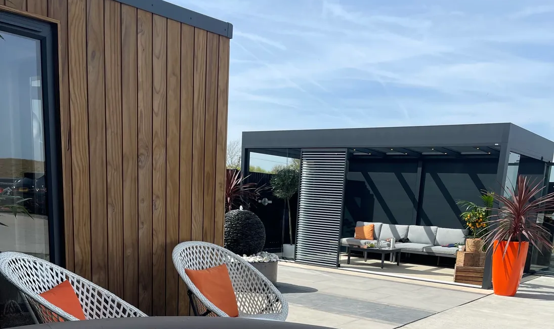 Modern outdoor space with hot tub, wooden garden room, cosy seating area, and vibrant patio plants under a clear sky