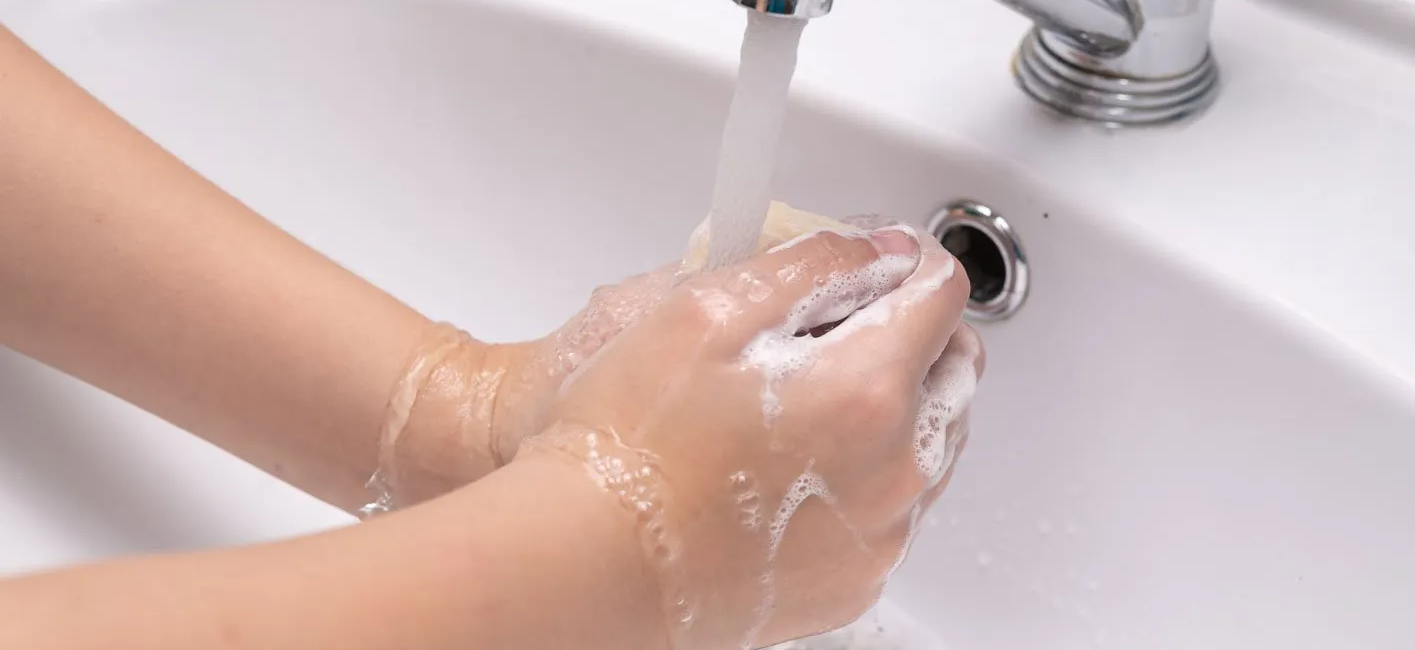 Hands washing with soap under running water in a white sink promoting hygiene and cleanliness