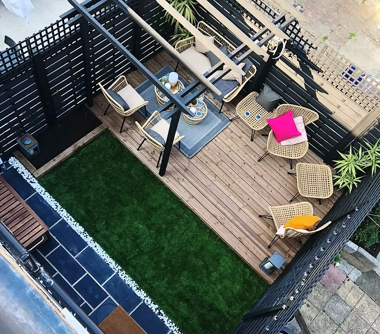 Top view of a stylish garden patio with wooden decking, wicker furniture, colourful cushions, and artificial grass lawn