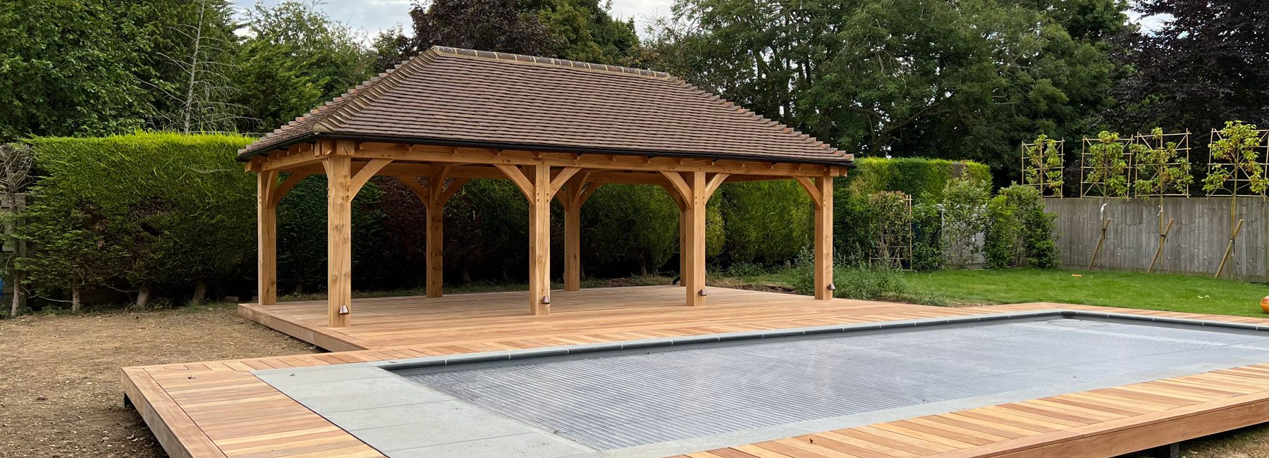 Wooden gazebo and modern swimming pool with timber decking in a lush garden setting