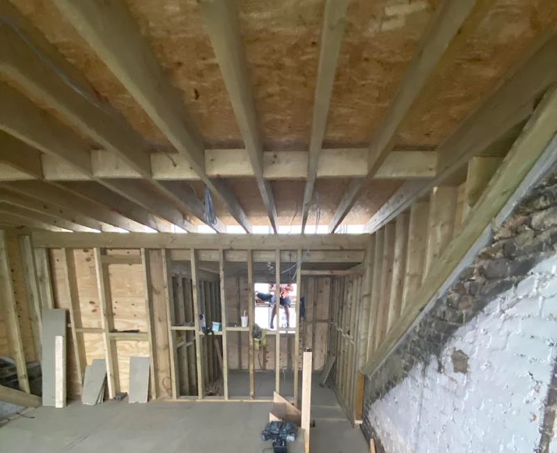 Wooden framework of an unfinished room with visible beams and exposed brick wall, under construction interior
