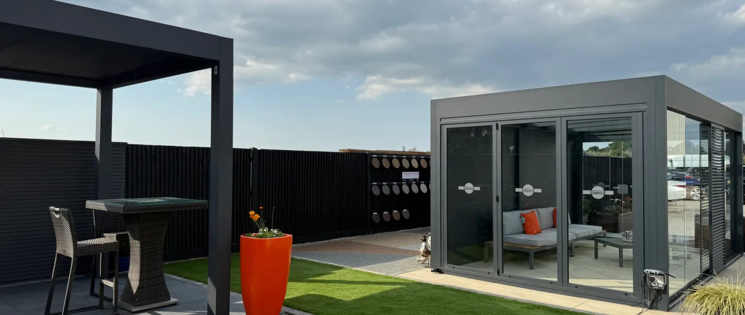 Modern garden with glass summerhouse, patio set, vibrant orange planter, and lush green lawn under a cloudy sky