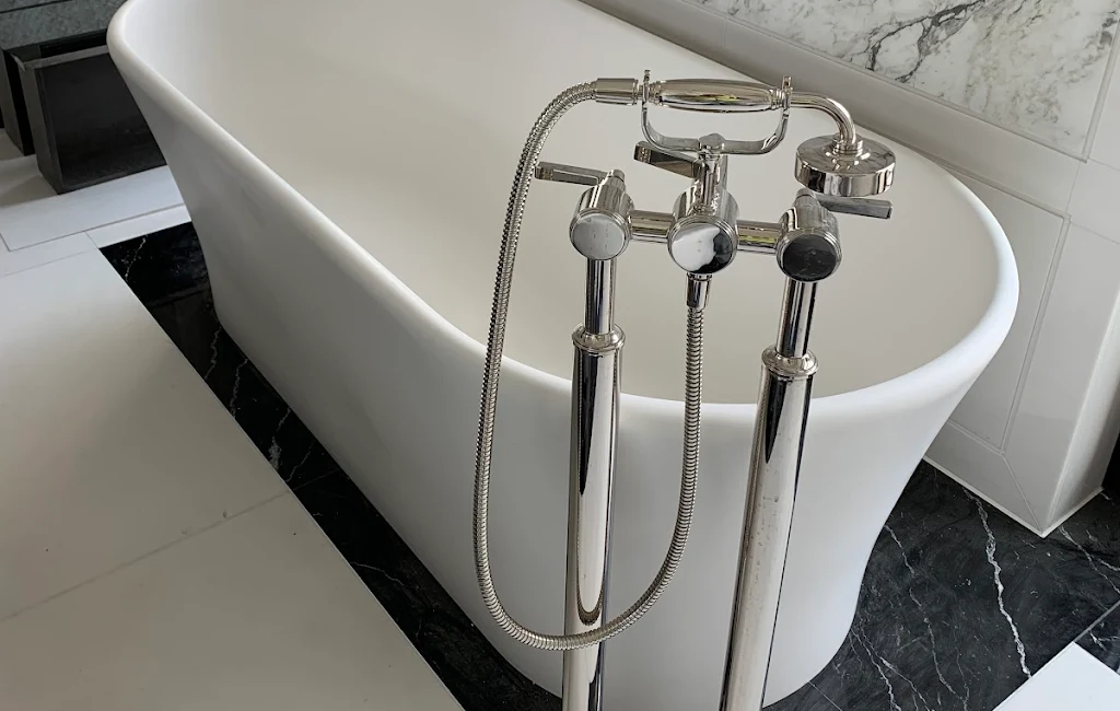 Freestanding white bathtub with chrome tap fixtures set on elegant black marble floor in modern bathroom design