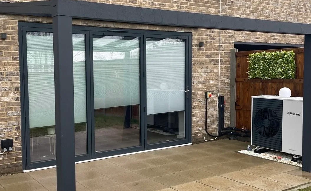 Modern house extension with glass doors and air source heat pump installation in a stylish brick exterior garden setting