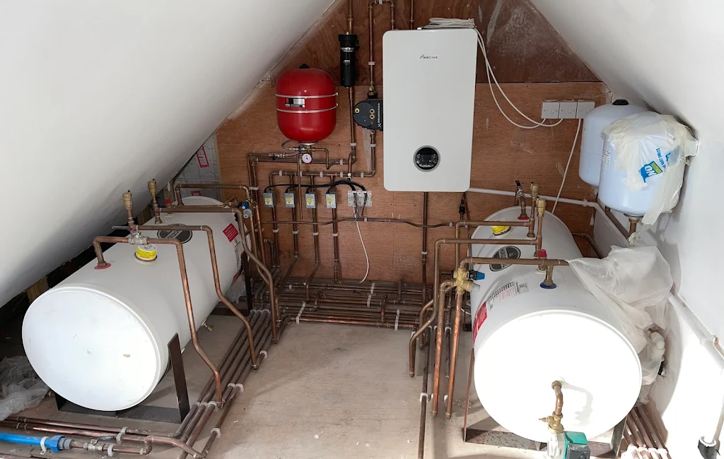 Home boiler system setup in attic with water tanks, red expansion vessel, and pipes, UK residential heating installation