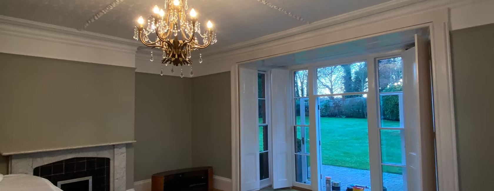Elegant living room with chandelier, fireplace, and garden view through large windows, decorated in soft neutral tones