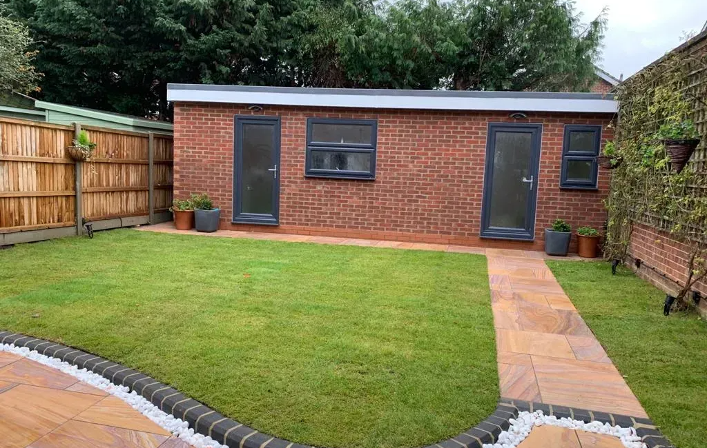 Garden with modern brick shed, patio path, and lawn surrounded by fencing and trees for privacy and aesthetics