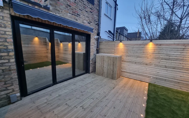 Modern wooden deck patio with ambient lighting and sliding glass doors in a cosy urban garden setting