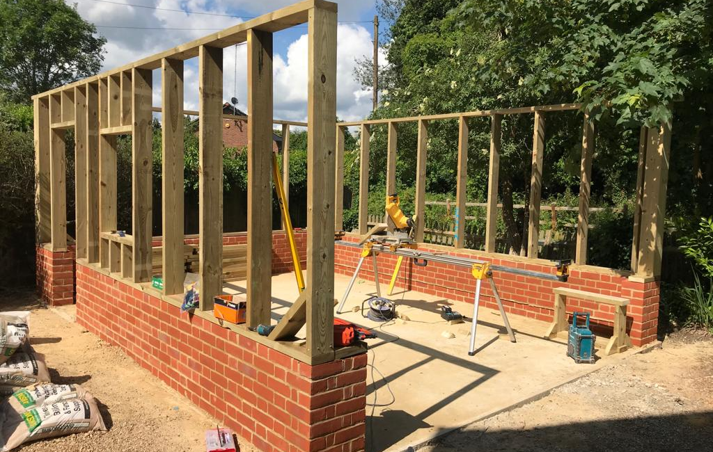 Wooden frame and brick structure under construction amidst trees and blue sky
