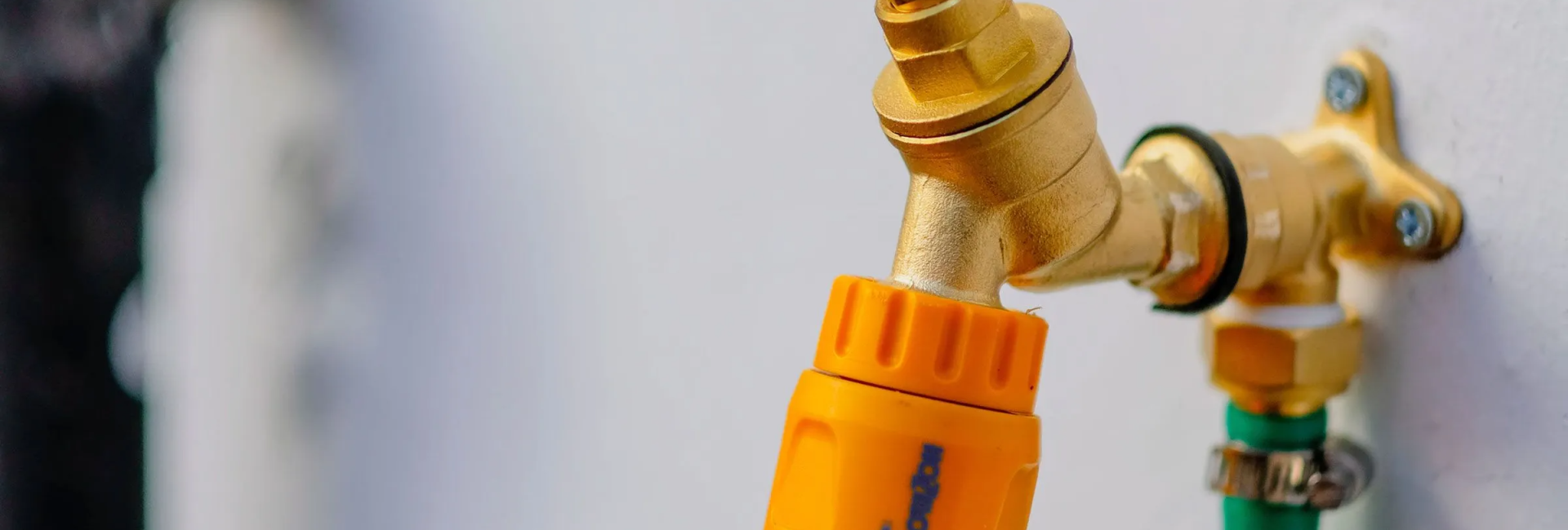 Close-up of a brass outdoor tap with yellow hose connector mounted on wall