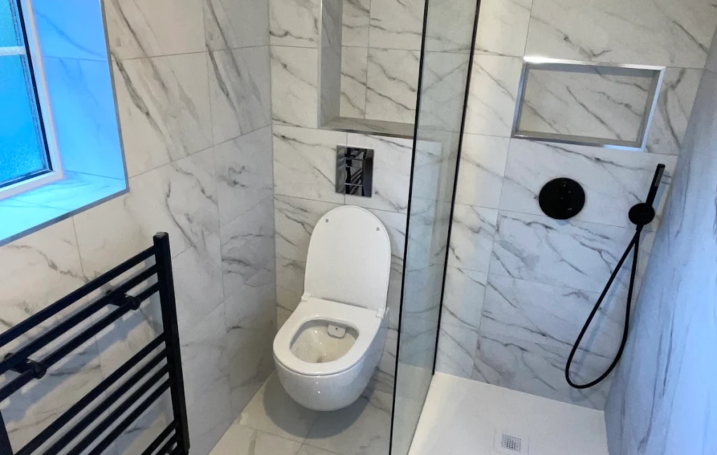 Modern bathroom with marble tiles featuring a wall-mounted toilet, walk-in shower, and black heated towel rail