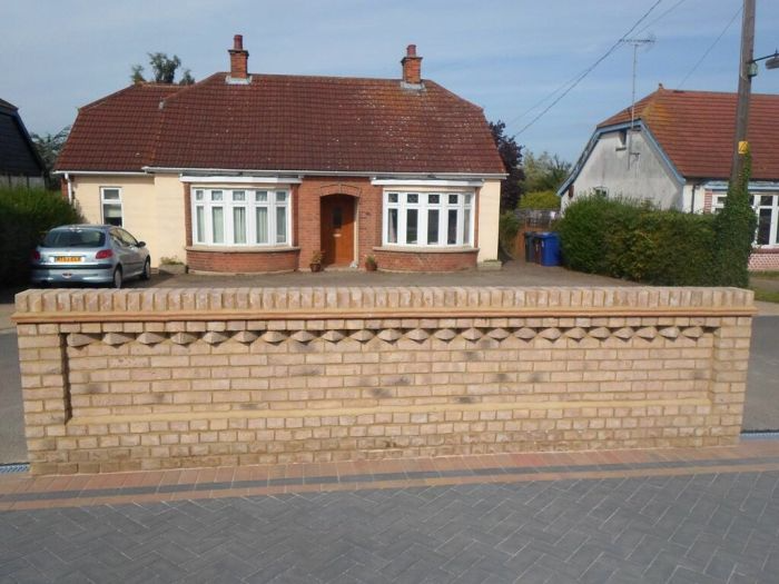 Red-roofed bungalow with brick wall, front driveway, and parked car in a suburban setting
