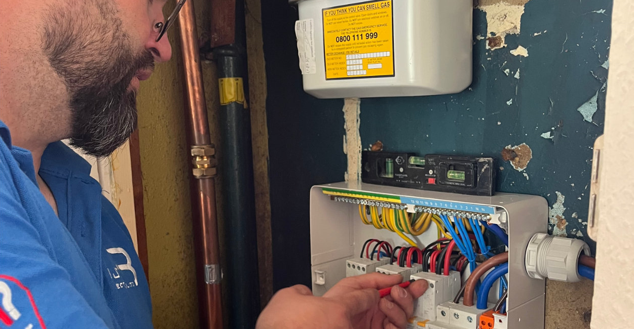 Electrician in blue shirt working on a distribution board wiring inside a building for maintenance or repair tasks