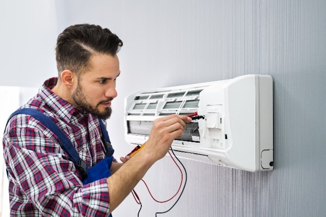 Technician repairing an air conditioning unit on a wall, wearing a plaid shirt and using tools