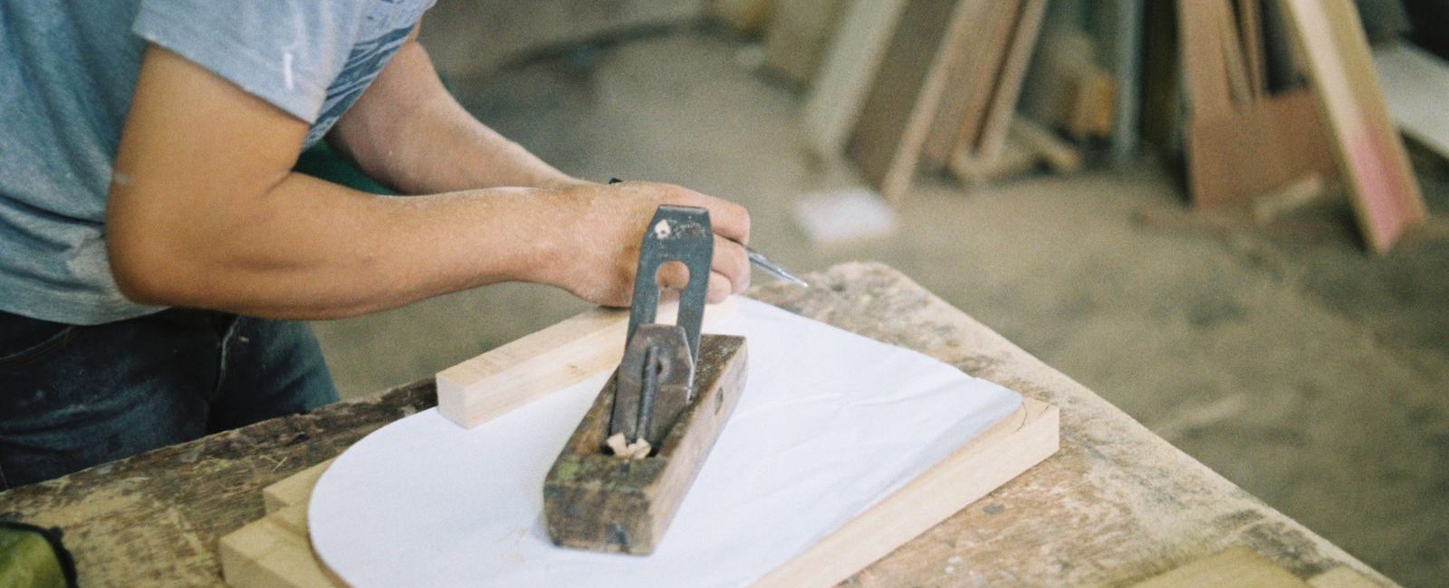 Carpenter woodworking with a hand plane on a wooden surface indoors.