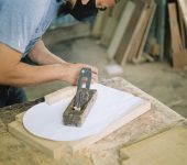 Carpenter woodworking with a hand plane on a wooden surface indoors.