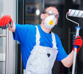 Painter wearing protective mask, goggles, and gloves holds paint roller ready for work indoors