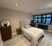 Modern bedroom with grey decor, wooden furniture, and large windows featuring a desk and chair setup for work or study