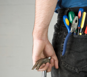 Man holding hammer with screwdrivers and pliers in back pocket of jeans, ready for DIY or repair tasks
