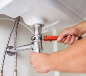 Plumber using a wrench to fix a sink pipe under a bathroom basin, showcasing plumbing repair and maintenance skills