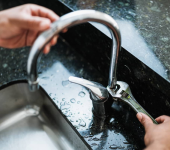 Person using a wrench to repair a leaking kitchen tap on a black countertop