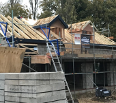 Construction site with partially built house featuring wooden roof trusses and scaffolding, surrounded by trees