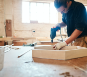 Carpenter using an electric drill on a wooden project in a sunlit workshop, highlighting craftsmanship and skill