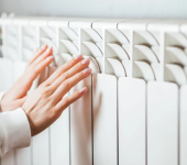Hands touching home radiator for warmth and comfort during cold weather