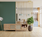 Modern living room with wooden furniture, green accent wall, floor lamp, and potted plant near a bright kitchen space