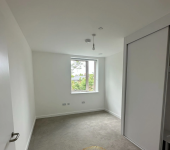 Modern minimalistic empty bedroom with white walls, grey carpet, and a window showcasing trees outside