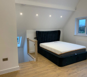 Loft bedroom with modern black velvet bed frame and cosy lighting, featuring wooden flooring and scenic window view