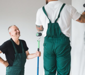 Two painters in green overalls painting a wall with grey paint while smiling at each other