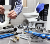 Plumber fixing sink pipe in bathroom with tools scattered on floor, demonstrating plumbing maintenance