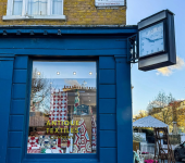 Storefront of Antique Textiles Company with a vintage clock and colourful quilts displayed inside a blue building