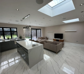 Modern open-plan kitchen and living area with marble flooring, skylights, and large windows overlooking the garden