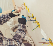 Electrician wiring outlets in wall, wearing gloves and plaid shirt, coiled cable on floor, working on electrical installation